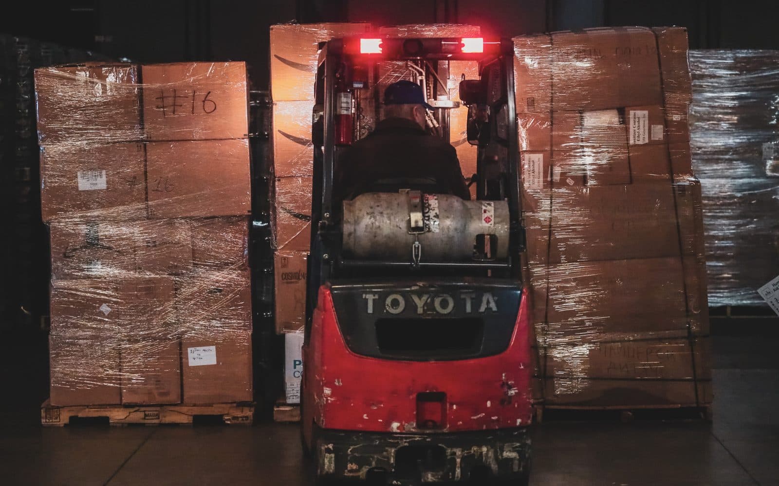 Red Toyota forklift between tall shrink-wrapped pallets of cardboard aid boxes in a warehouse